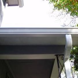 Tucker's Home Services — finished white aluminum seamless gutter installed along a roofline with clean downspout termination